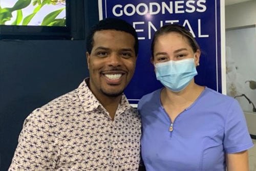 Smiling man and woman in front of Goodness Dental sign